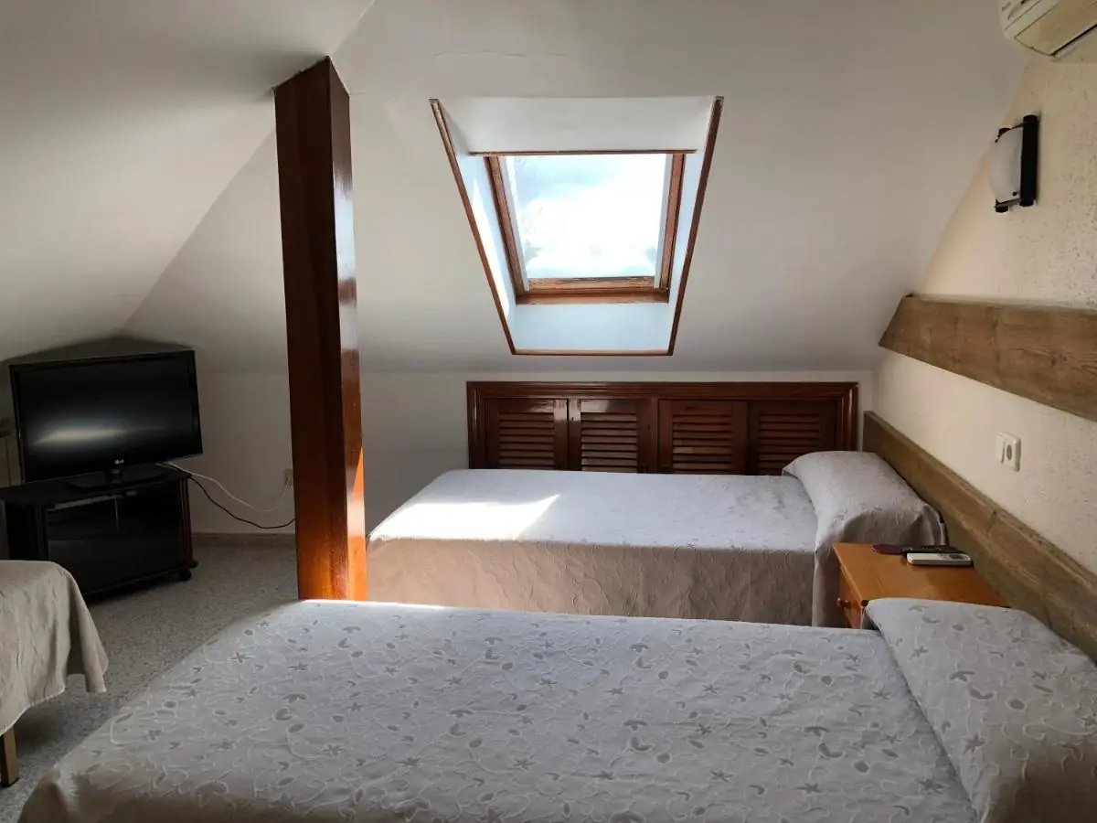Habitación triple abuhardillada con tres camas, televisión y ventana al tejado